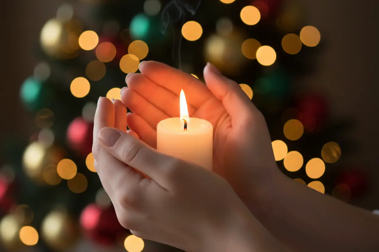 Mãos segurando vela acesa, luzes de Natal ao fundo, simbolizando mensagens de natal para clientes.
