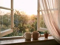 Two mugs of coffee on a windowsill bathed in the golden light of dawn