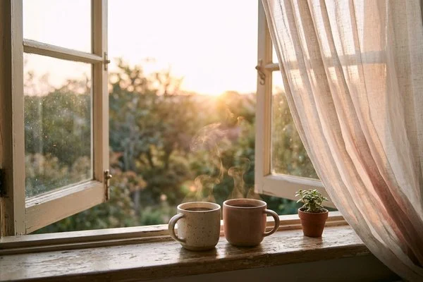 Duas canecas de café sobre uma janela aberta com luz dourada do amanhecer